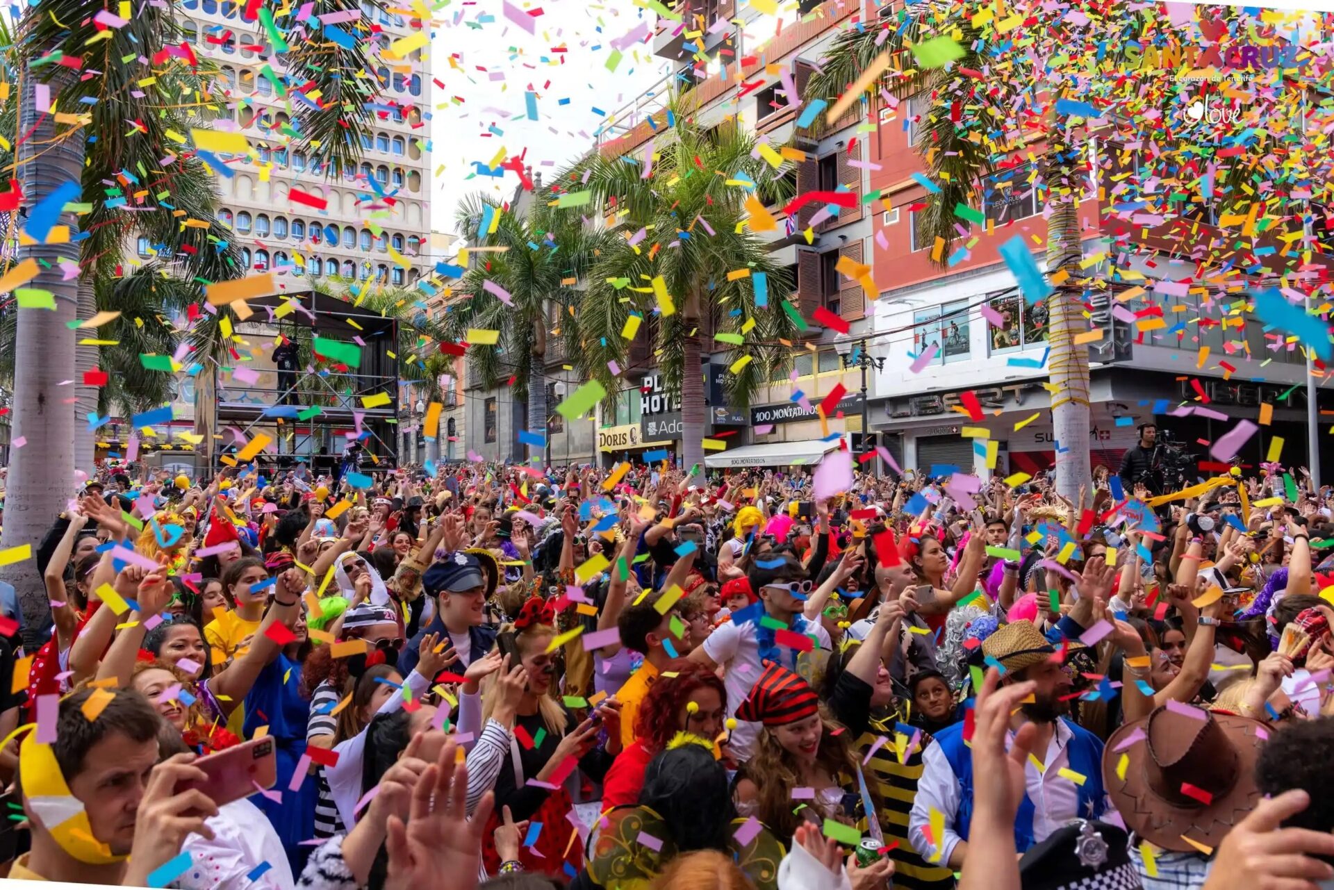 Crowds in carnival costumes celebrating under colorful falling confetti at the Tenerife Carnival.